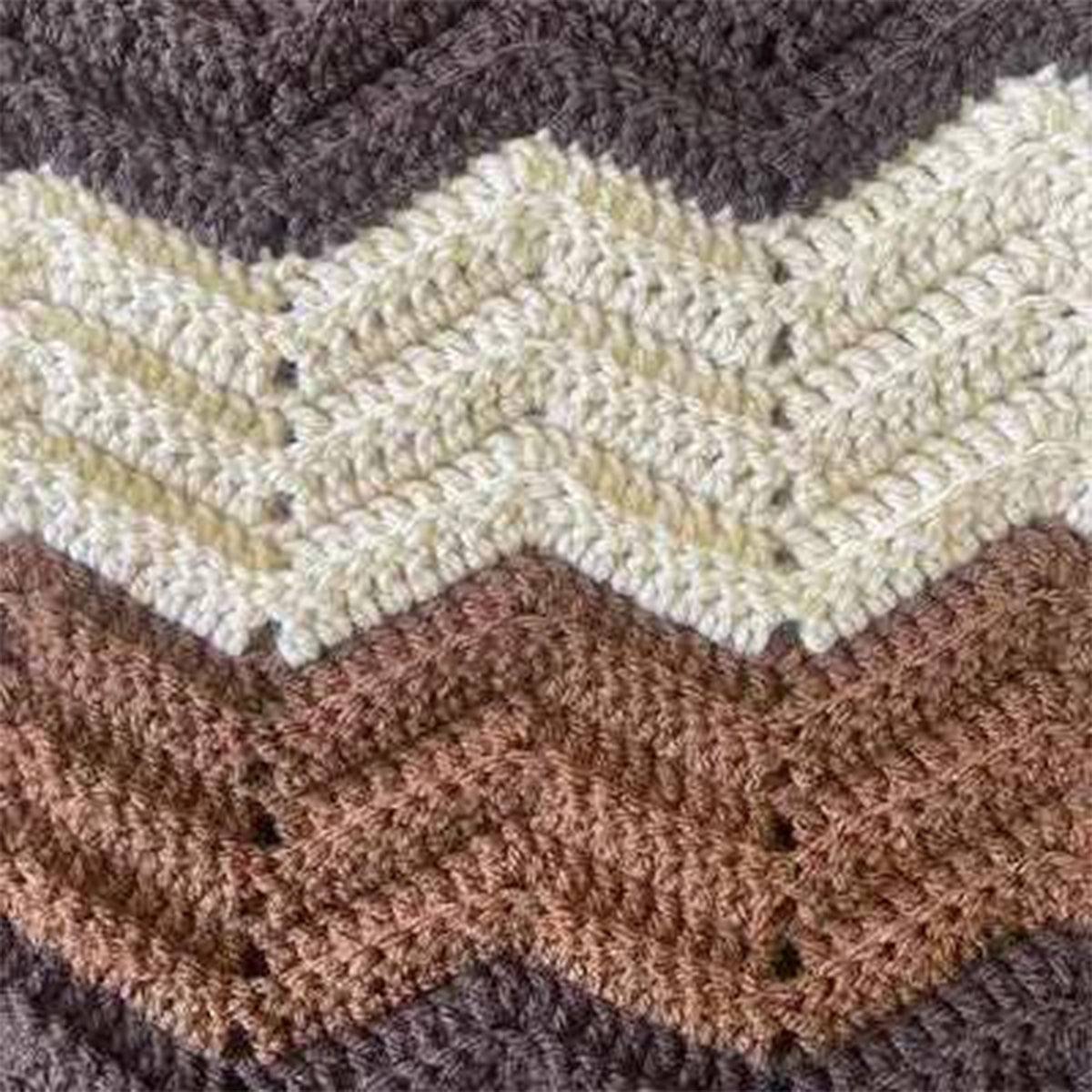 Close-up of a crocheted or knitted chevron pattern with alternating zigzag bands in dark brown, cream, tan, and medium brown.