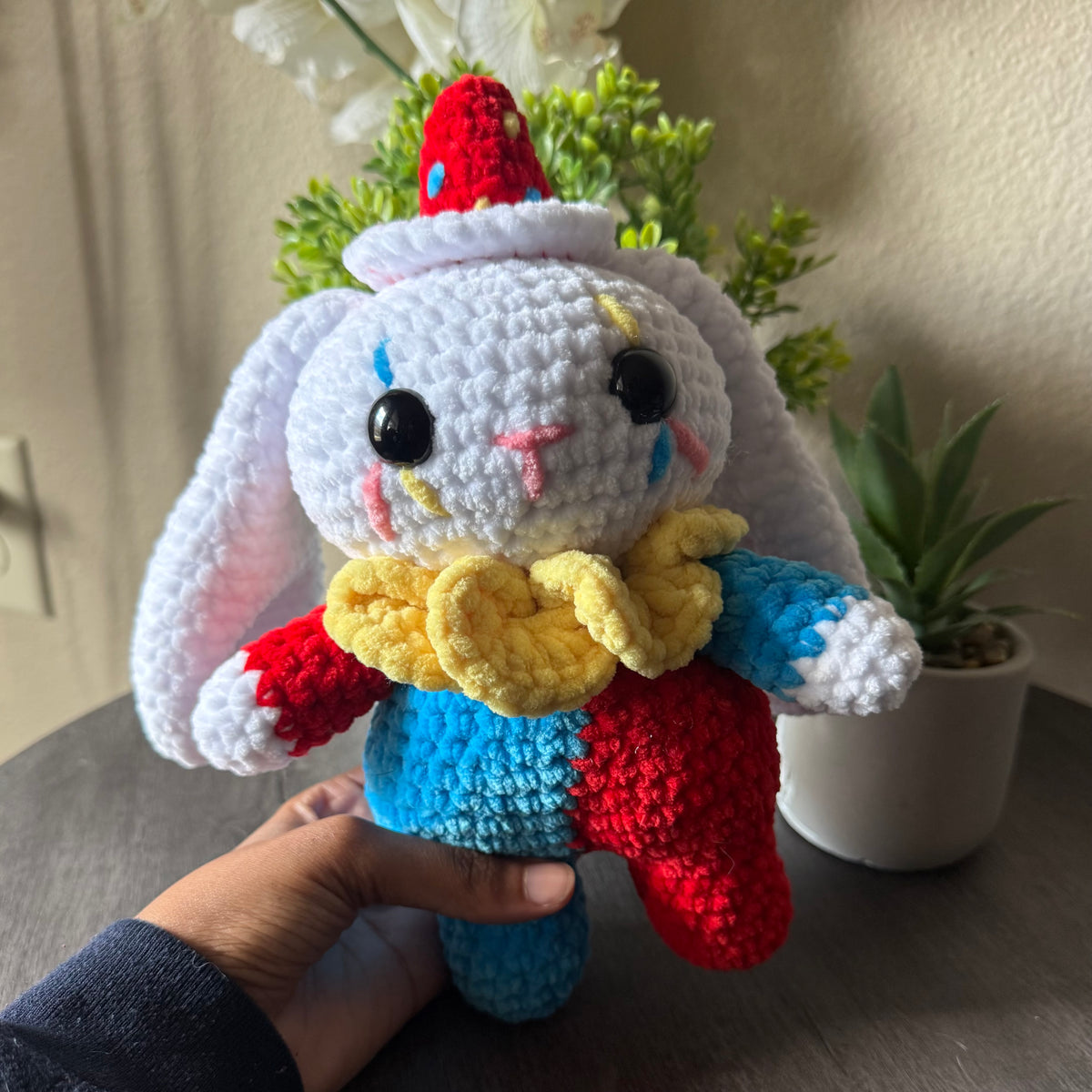Colorful crocheted bunny toy held by a hand with plants in the background