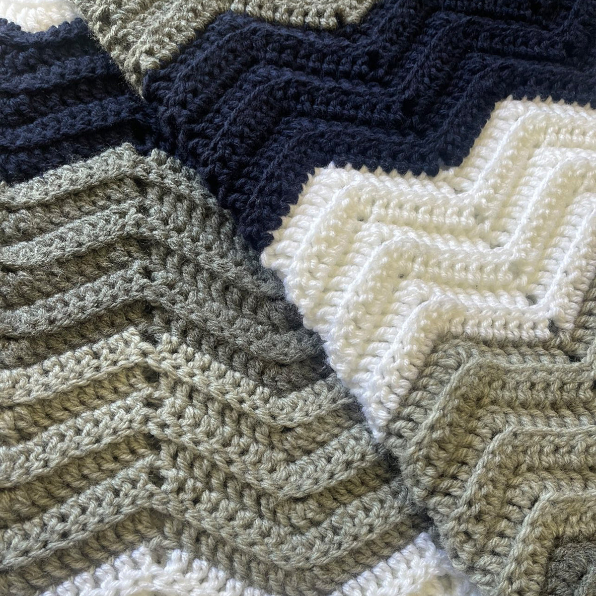 Close-up of a crocheted textile with a chevron pattern in dark navy, cream, and warm gray-beige yarns.