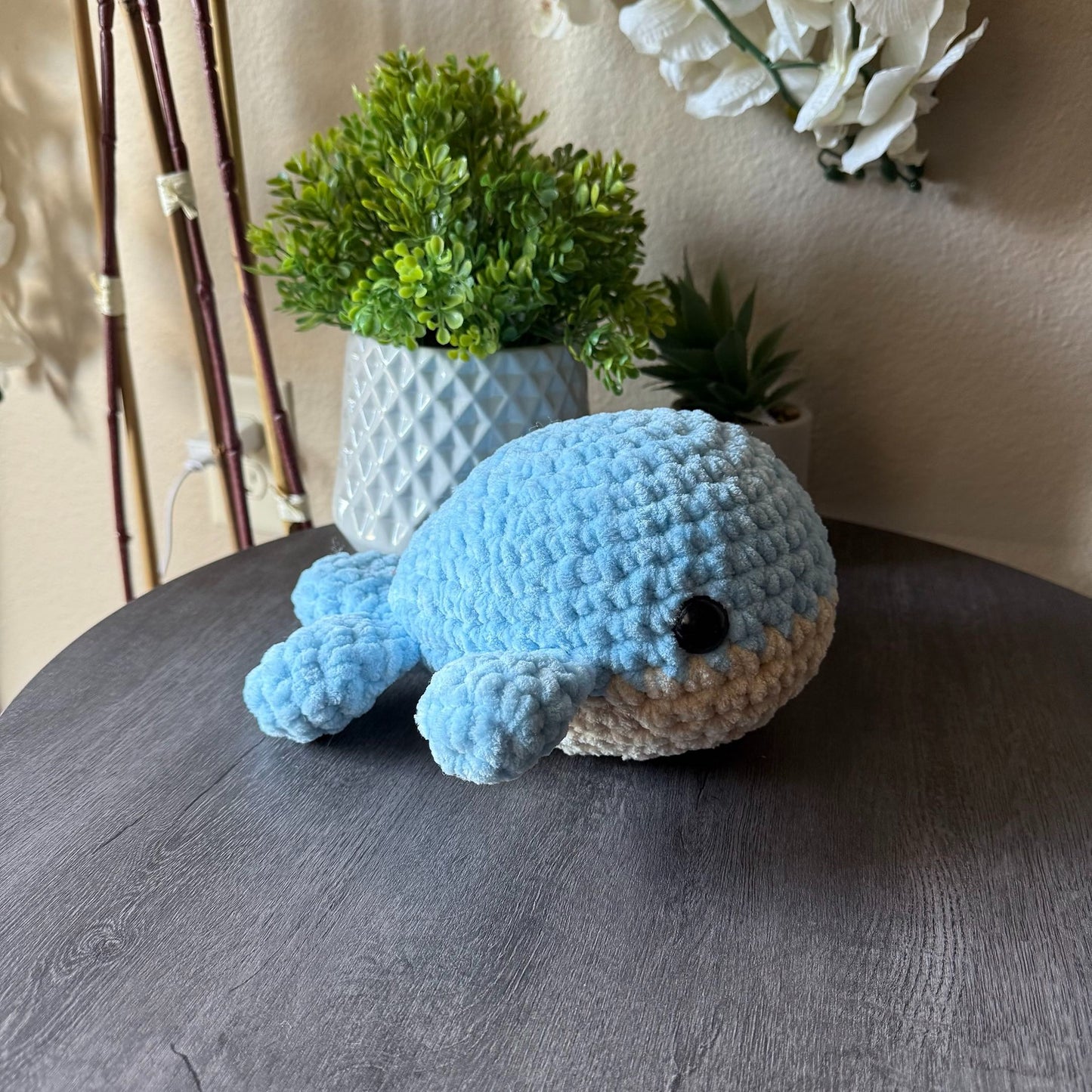 Blue crochet whale toy on a wooden surface with plants in the background