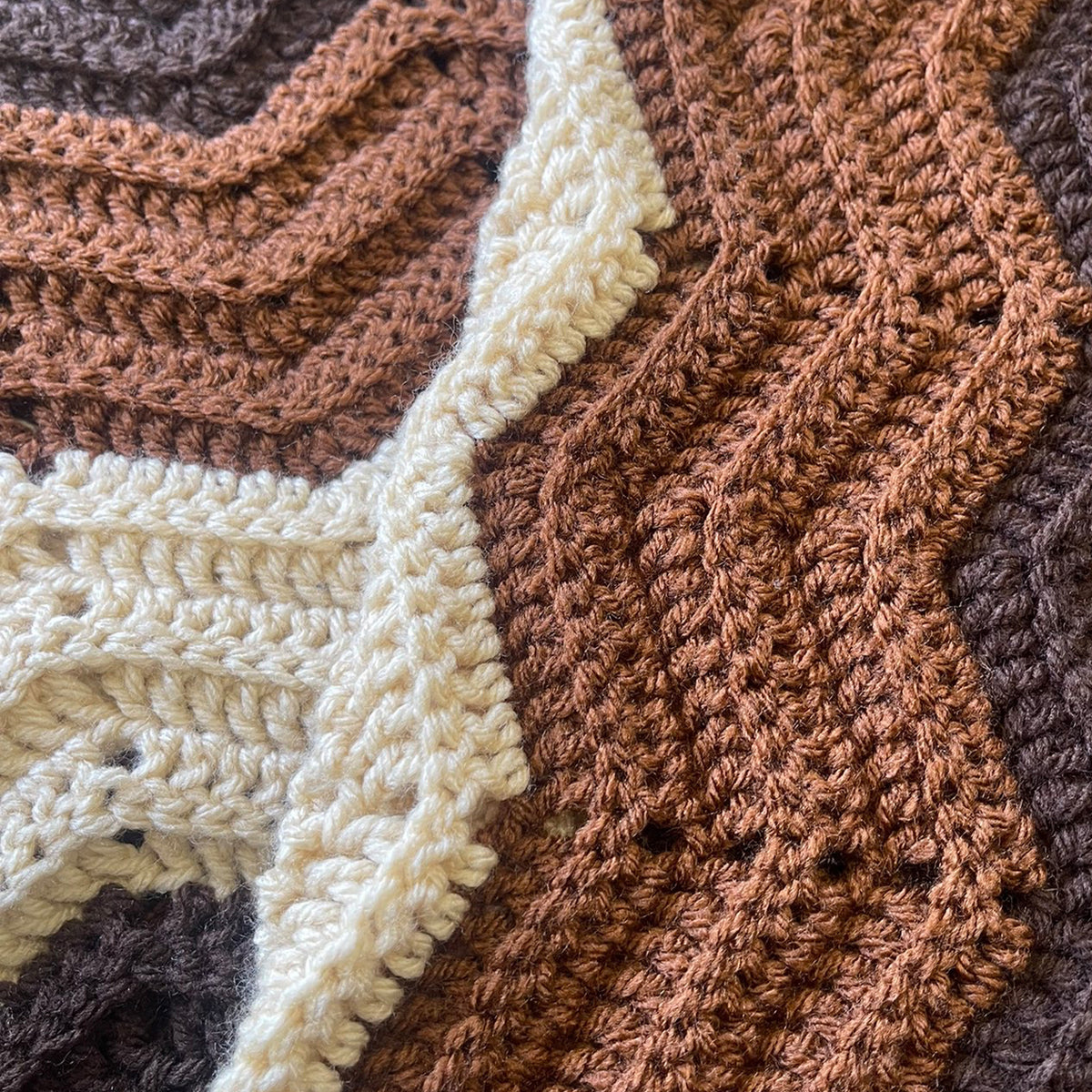 Close-up of a crocheted textile with textured zigzag panels in warm brown, cream, and dark taupe tones.