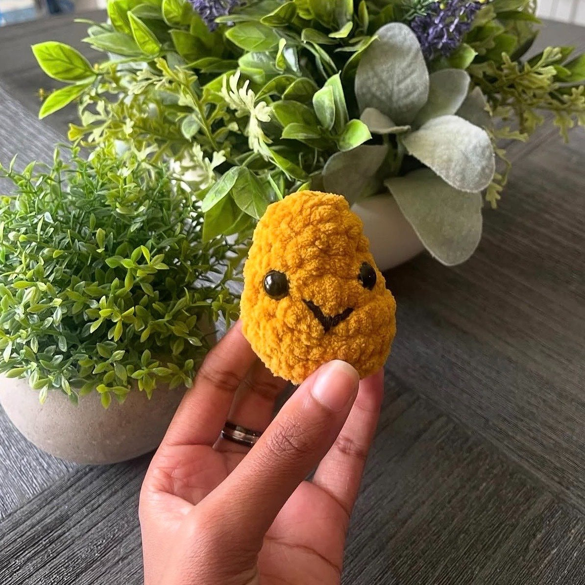 Hand holding a chicken nugget plushie with plants in the background