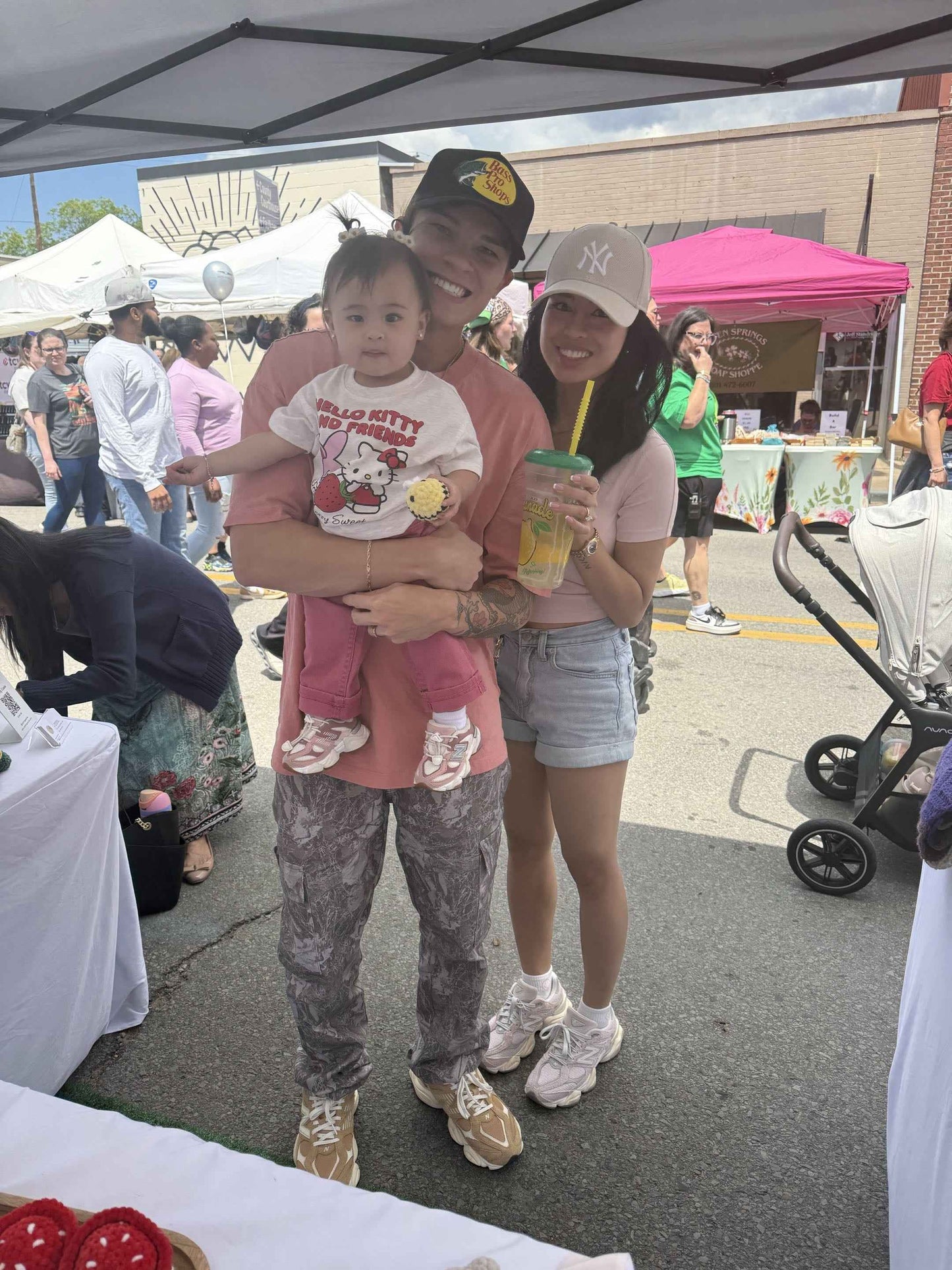 Family of three at an outdoor event with tents and people in the background