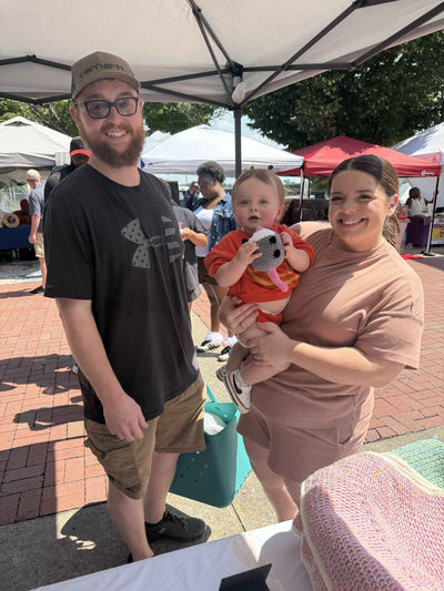 Family of three at an outdoor event under a white canopy