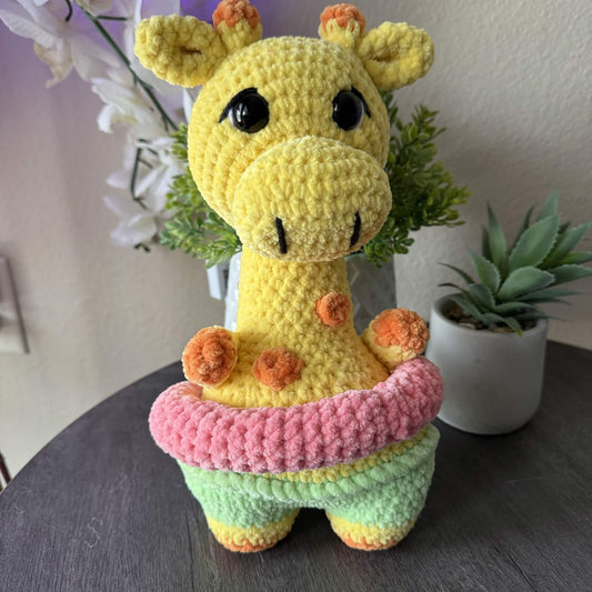 Crocheted giraffe toy with a pink floatie on a table with plants in the background