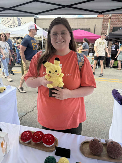 Person holding a plush toy at an outdoor event with booths and people in the background