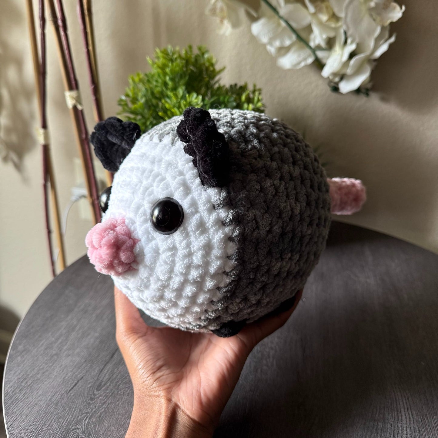 Hand holding a jumbo opossum plushie with a neutral background