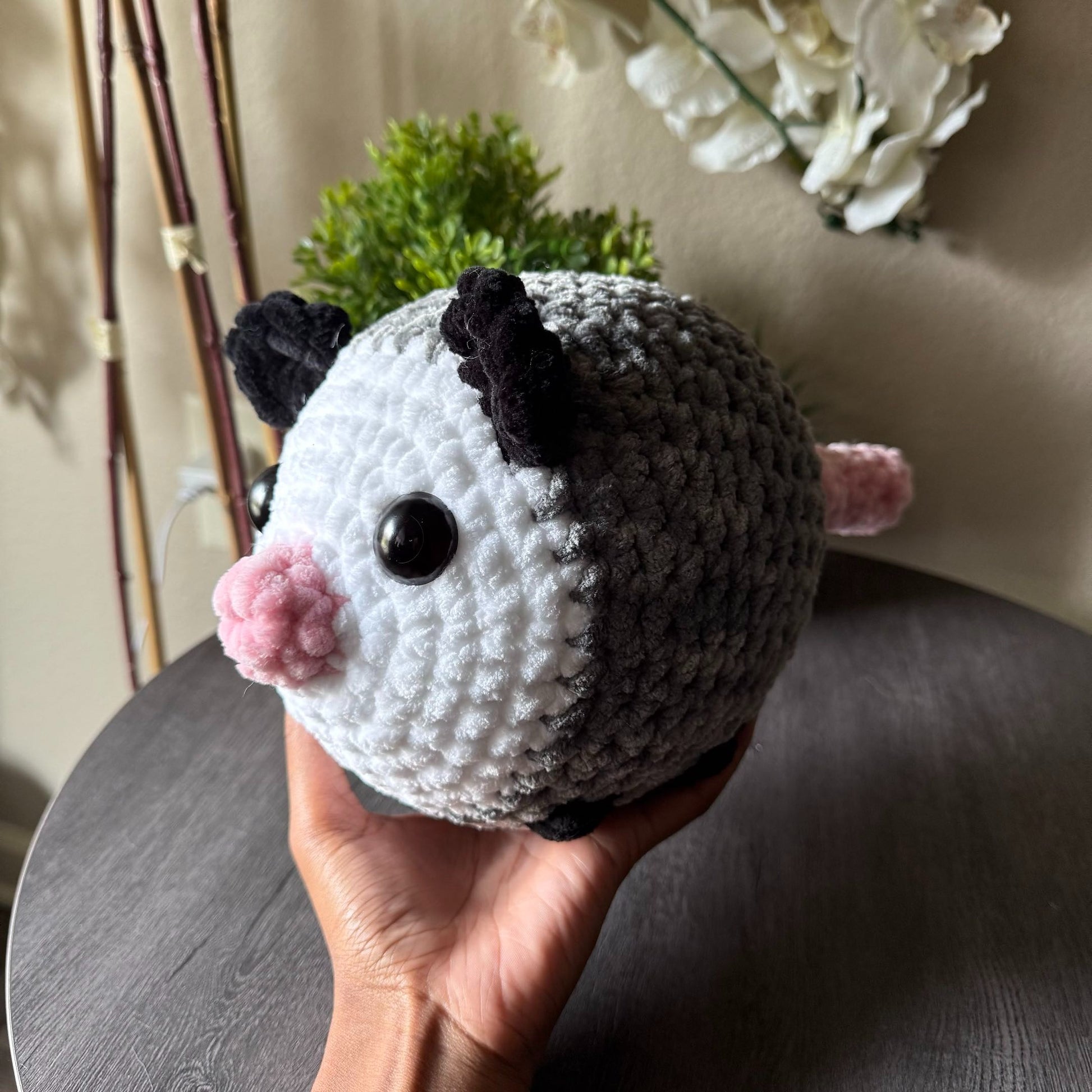 Hand holding a jumbo opossum plushie with a neutral background