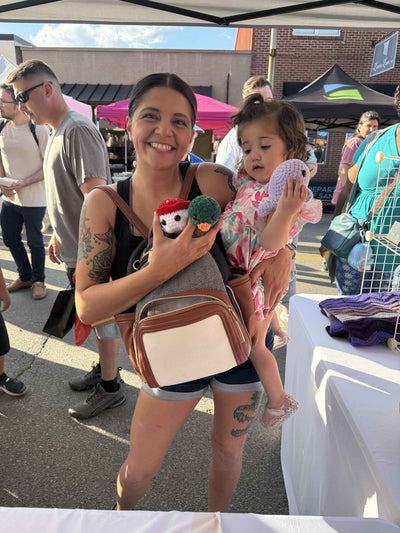 Woman holding a child at an outdoor event with people and tents in the background