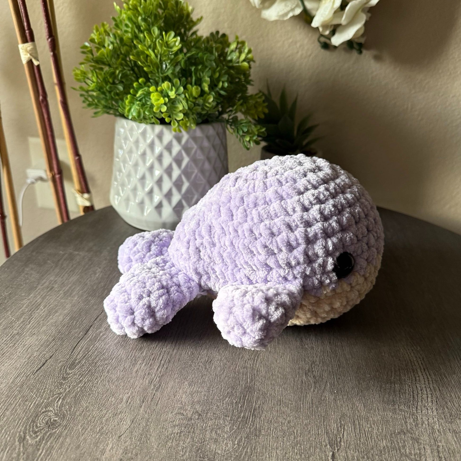 Crocheted purple animal toy on a wooden surface with a plant in the background
