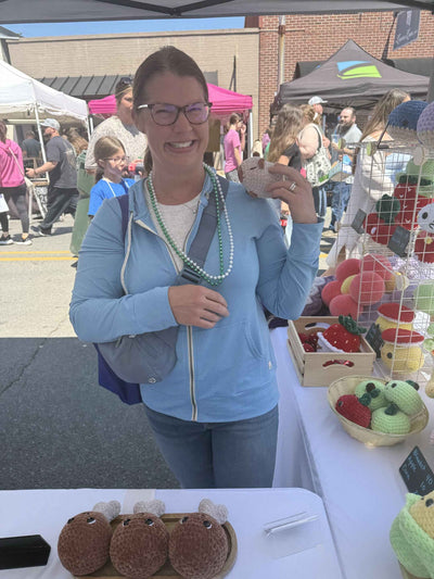 Woman taking a selfie at an outdoor market with various stalls and people in the background